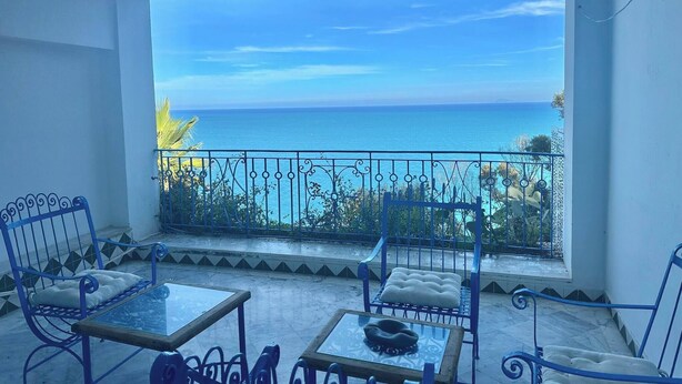 Un balcon donnant sur la mer, aménagé avec des chaises et une table en métal.