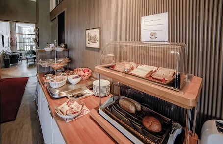 A buffet with various food items, a framed picture on the wall, and a sign with menu items.. Jugend Boutique Hotel