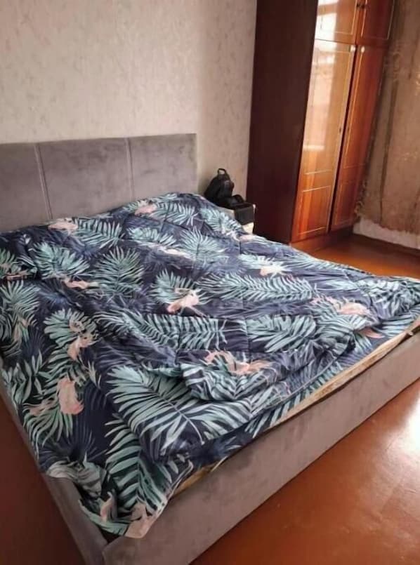 A bed with a floral bedspread, a headboard, and a wooden floor.
