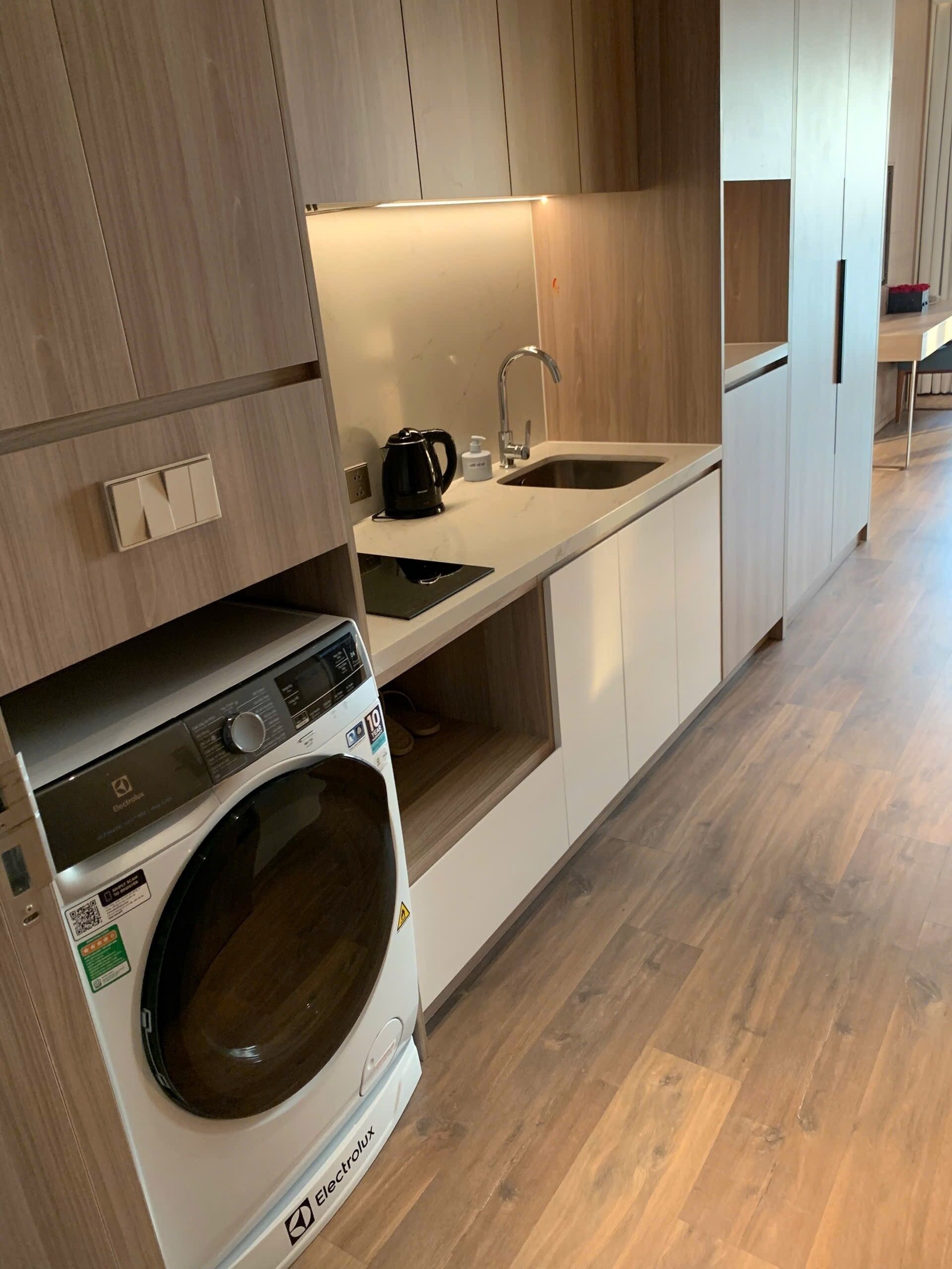 A modern kitchen with a built-in washer and dryer, a sink, and wooden cabinetry.