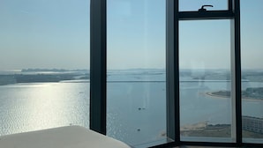 Une chambre moderne dotée d’une grande fenêtre donnant sur une étendue d’eau et sur un paysage lointain.