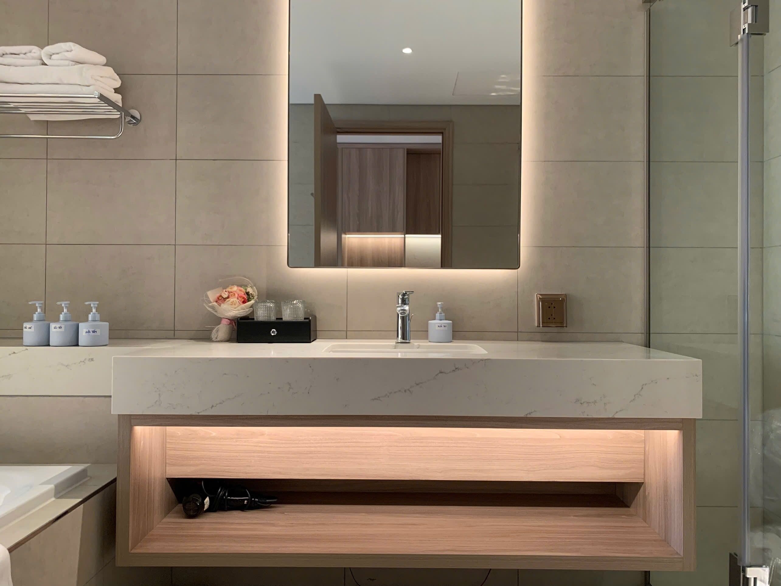 Un baño moderno con un espejo grande, un lavabo de mármol y un mueble de tocador de madera.