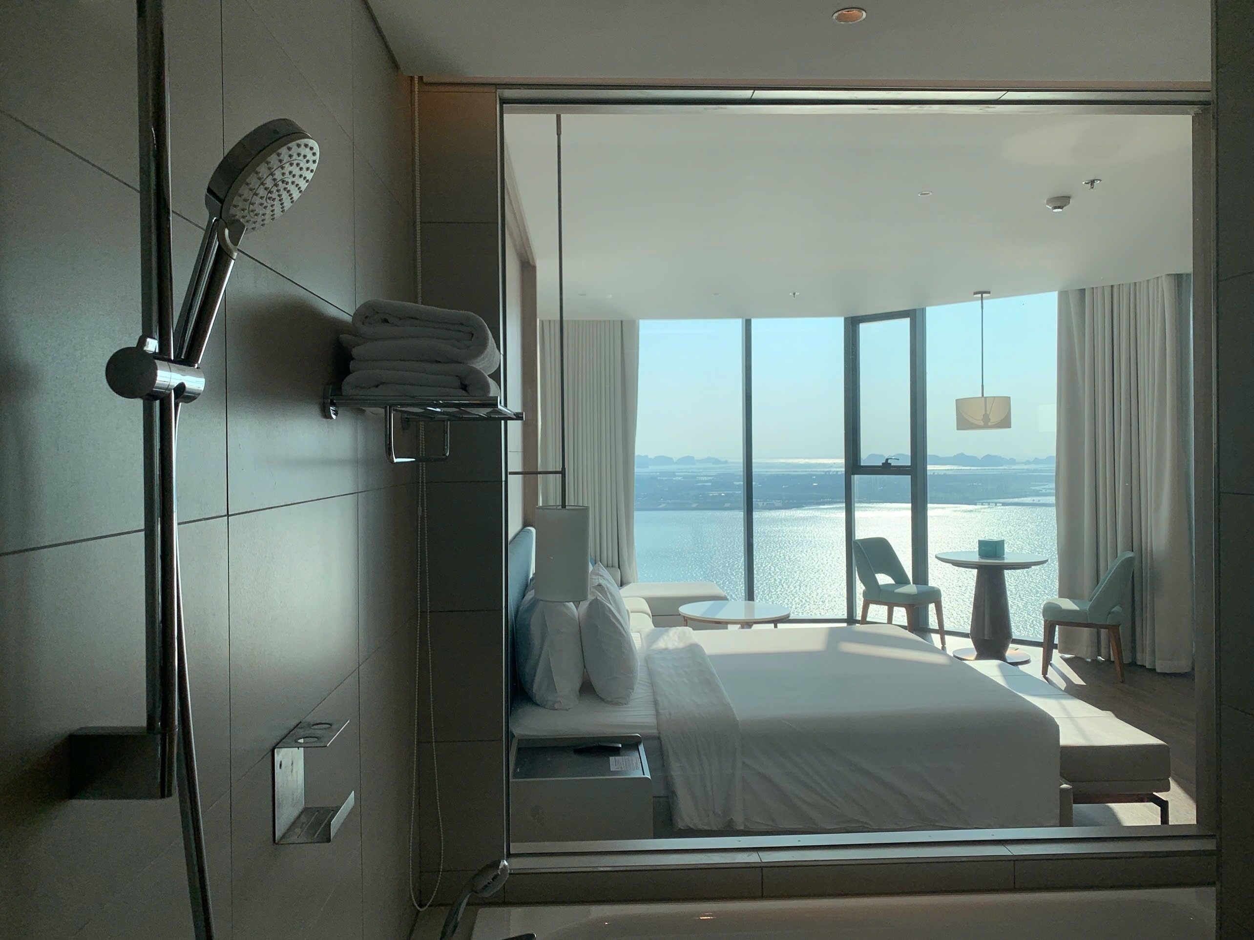 Une chambre d’hôtel moderne dotée d’un grand lit, d’une douche, d’un balcon avec vue sur l’eau et d’un coin salon avec une table et des chaises.