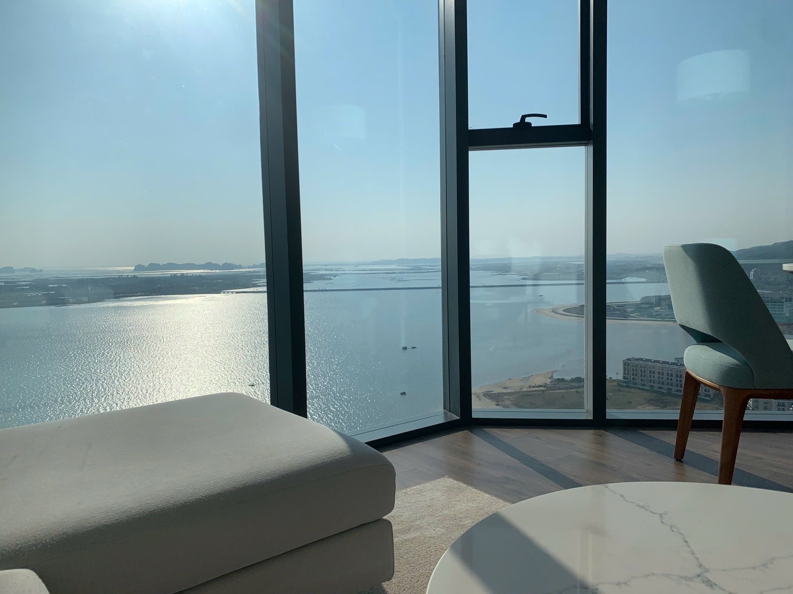 Quarto moderno com uma janela grande que oferece vista para um rio e paisagem distante.