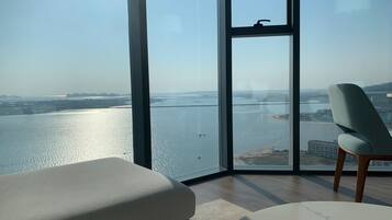 Quarto moderno com uma janela grande que oferece vista para um rio e paisagem distante.