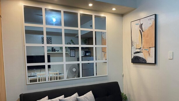 Una sala de estar moderna con un sofá negro, un ventanal de varios paneles y un cuadro abstracto enmarcado en la pared.