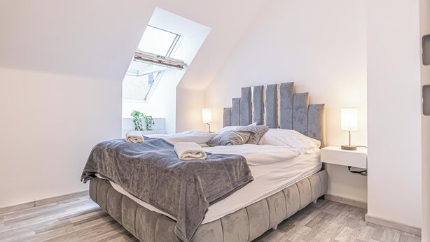 Camera da letto moderna con finestra a lucernario, un letto con testiera grigia e lampade da comodino.