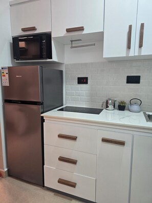 Una cocina moderna con un refrigerador de acero inoxidable, un microondas, un lavamanos y una estufa. Los gabinetes tienen pomos de madera y hay una pequeña planta en maceta sobre la encimera.