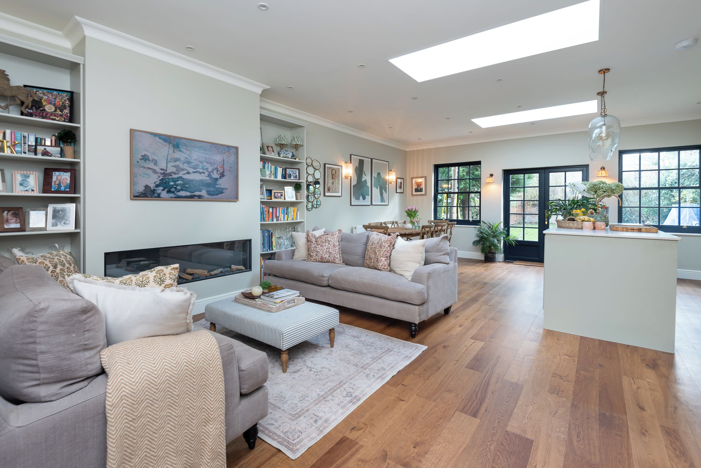 A spacious living room with a fireplace, a sofa set, a coffee table, and a bookshelf filled with books and decorative items.