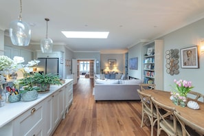 A spacious kitchen with white cabinets, a central island, and a dining area with a wooden table and chairs. - Beautiful 5BDR 3Bath Home in Barnes (Greater London)