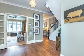 A spacious foyer with a wooden floor, a staircase, and a view into a living area with a sofa and a window. - Beautiful 5BDR 3Bath Home in Barnes (Greater London)
