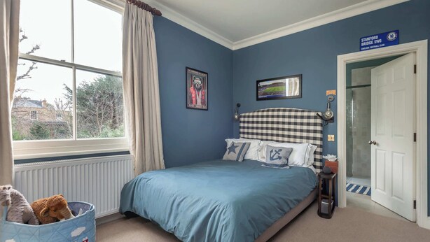 Une chambre à coucher avec un lit, une fenêtre avec des rideaux, un tableau accroché au mur et une porte.