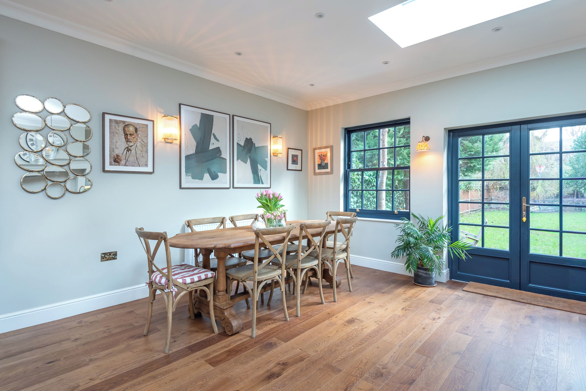 A dining area with a wooden table and chairs, surrounded by artwork and wall-mounted lights.