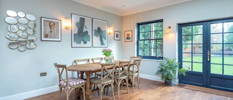 A dining area with a wooden table and chairs, surrounded by artwork and wall-mounted lights.
