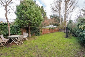 Ein Garten mit Holztisch und -stühlen, einem großen Baum und einem Holzzaun.