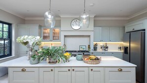 Une cuisine dotée d’un îlot central, de luminaires suspendus, d’une horloge et d’un réfrigérateur.