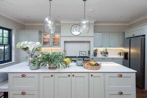 A kitchen with a central island, pendant lights, a clock, and a refrigerator. - Beautiful 5BDR 3Bath Home in Barnes (Greater London)