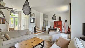 Ein geräumiges Wohnzimmer mit einer Couch, einem Couchtisch und Dekorationselementen. Eine Treppe führt in einen oberen Bereich, und ein rotes Schränkchen ist zu sehen.