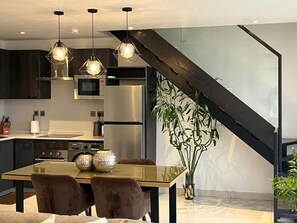 A modern kitchen with a dining area, featuring a staircase, stainless steel appliances, and pendant lighting. - Exclusive 2-bedroom penthouse at The Lennox, Airport Residential Area (Accra)