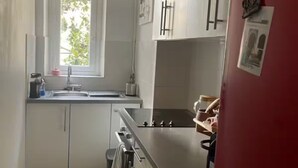 Eine Küche mit weißen Schränken, einem roten Kühlschrank, einem Fenster und einer hängenden Pendelleuchte.