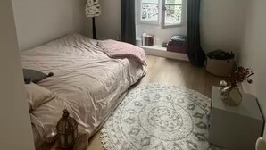Ein Schlafzimmer mit einem Bett, einem runden Teppich, einem kleinen Tisch mit einer Laterne und einem Fenster mit Vorhängen.