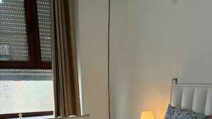 Ein ordentlich bezogenes Bett mit einer blauen und weißen Bettdecke, ein aufgerolltes weißes Handtuch und eine Nachttischlampe auf einem Nachttisch.