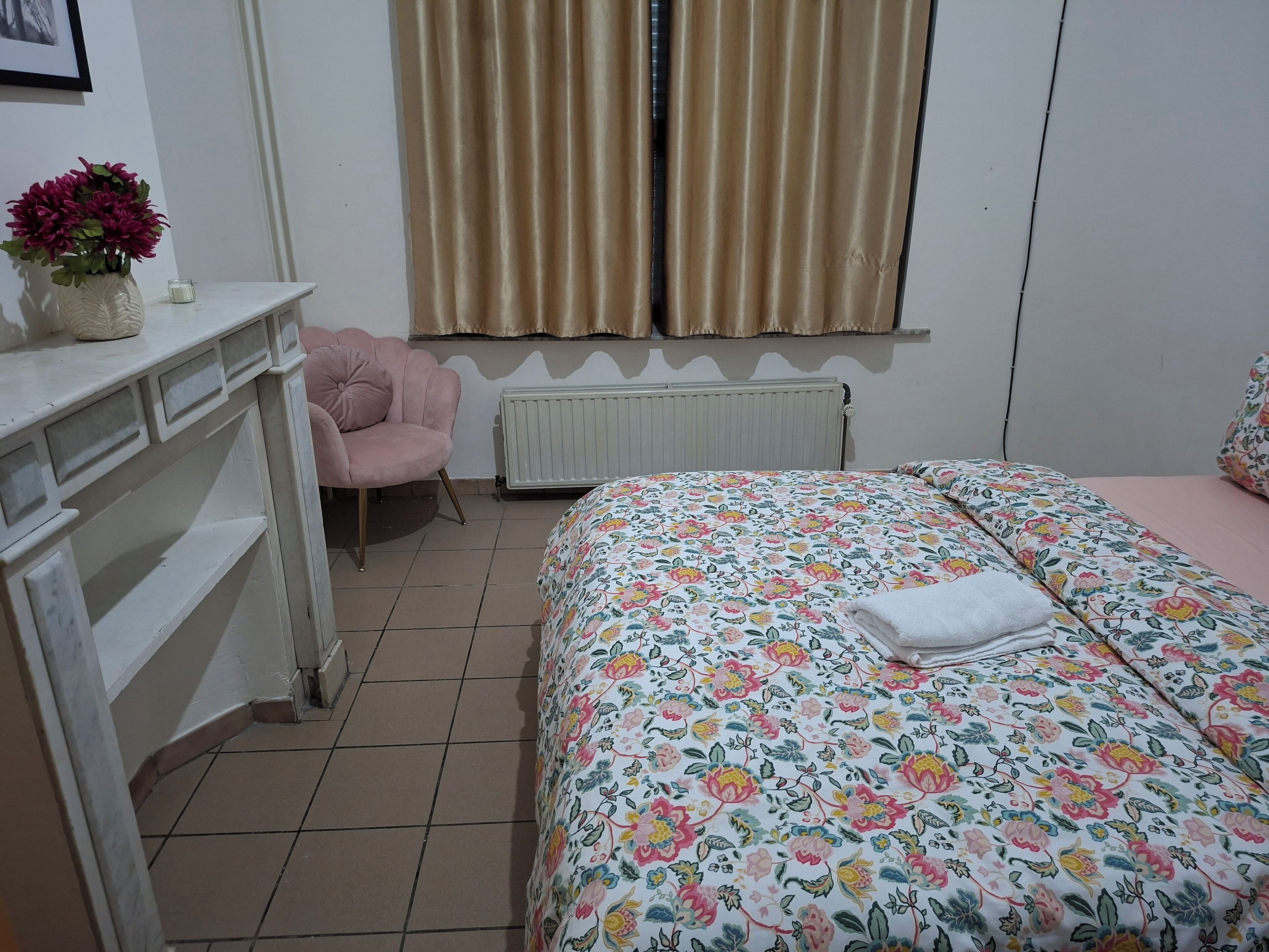 A bedroom with a bed, a desk, a chair, a radiator, and a window with curtains.