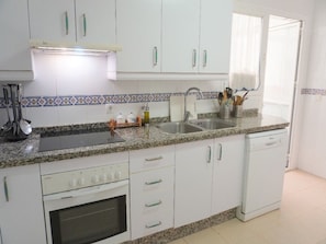 A kitchen with white cabinets, a granite countertop, a sink, a stove, and a dishwasher. - Bright apartment with terrace, swimming pool and parking | Up to 6 guests (Fuengirola)