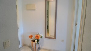 Un couloir doté d’un plancher en bois, d’un miroir au mur et d’une petite table ornée de fleurs.
