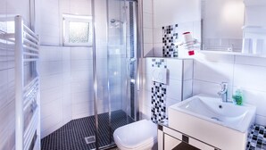 Un bagno moderno con box doccia in vetro, un water bianco e un lavandino con specchio sopra.