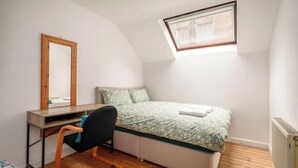 Et værelse indrettet i kollegiestil med en køjeseng, et skrivebord med stol, et spejl og en radiator.