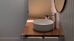 Un bagno con un lavandino tondo, un piano d'appoggio in legno e due piante in vaso su uno scaffale.