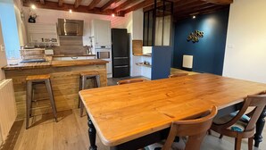 Una cocina moderna con encimeras de madera, una isla central y taburetes de bar. Hay un comedor con una gran mesa y sillas de madera.