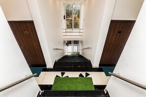 Interior moderno de un hotel con una escalera central, un extintor y vistas al exterior a través de un amplio ventanal.