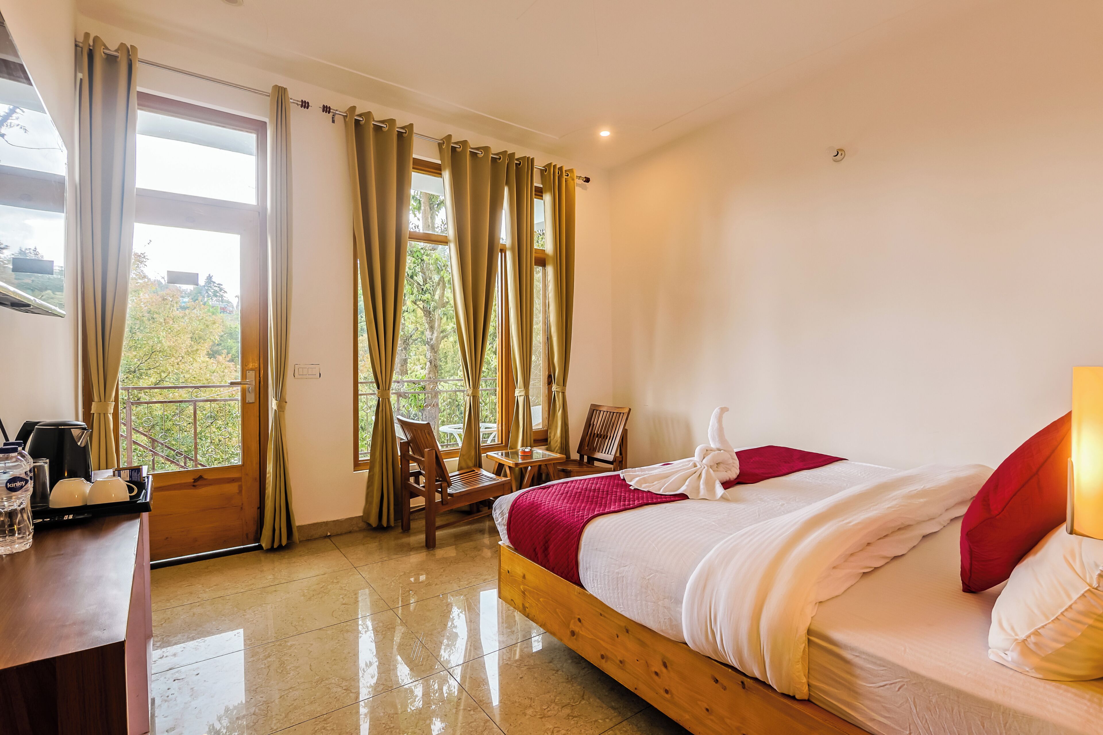 A hotel room with a bed, a desk with a coffee maker, a chair, a table, and a window with curtains.