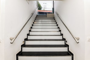 Una escalera con peldaños blanco y negro, barandillas de metal y vista al exterior.