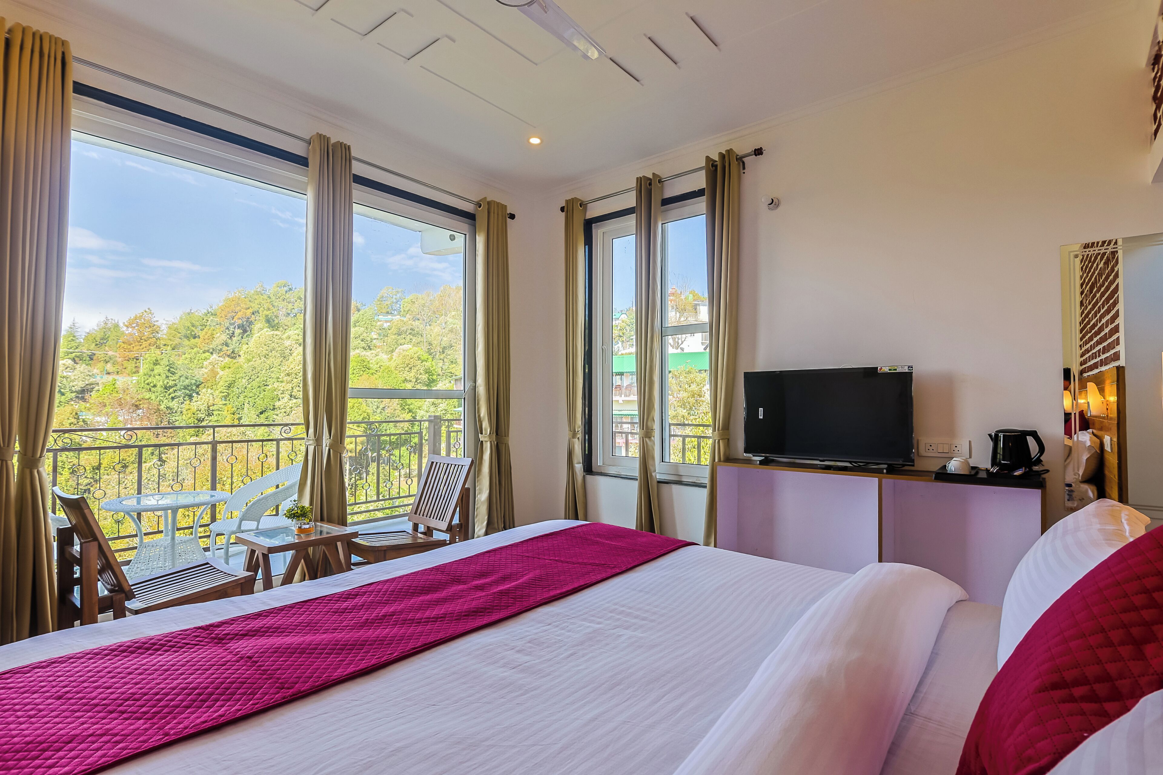 A hotel room with a bed, a TV, a balcony with chairs, and a table.