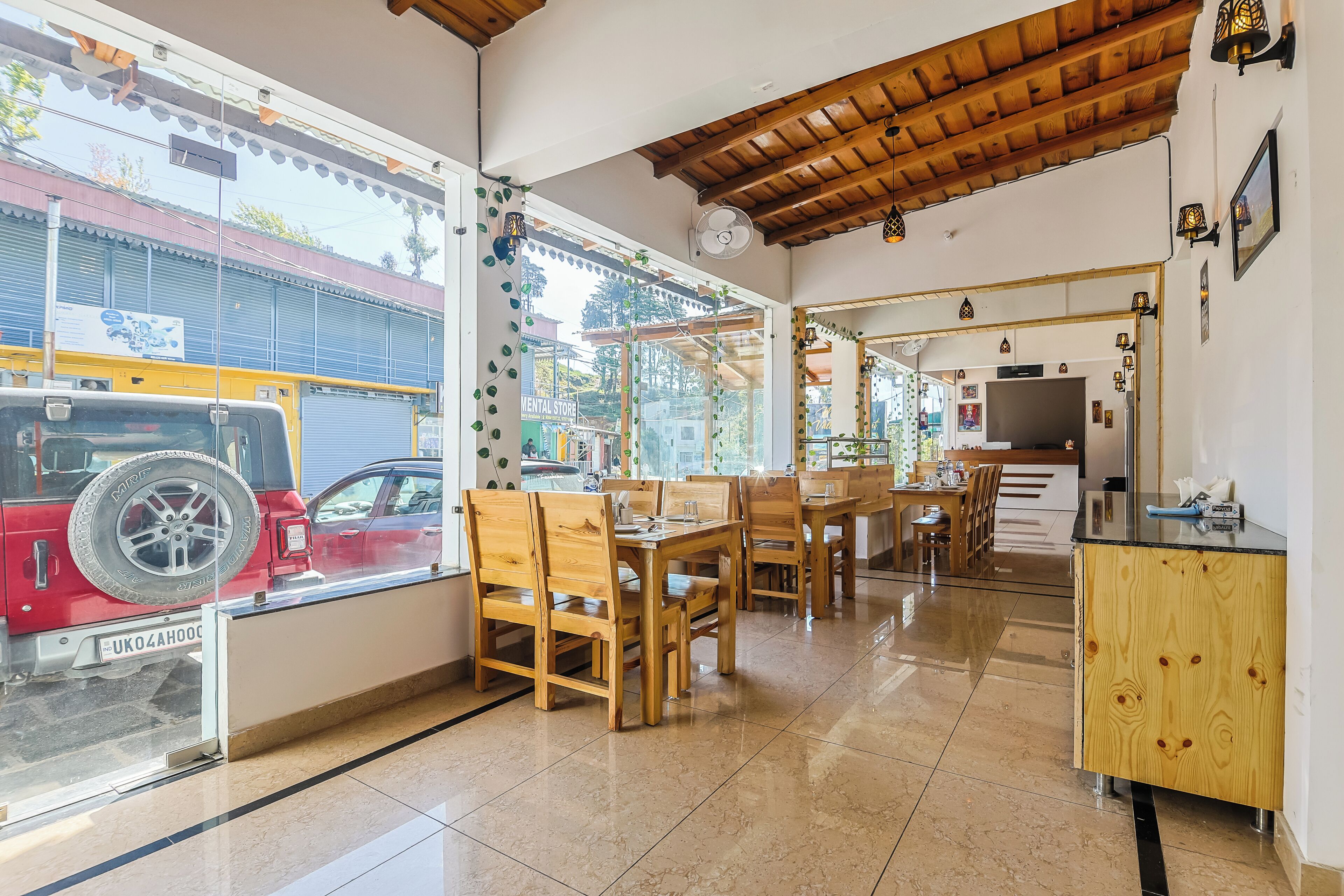 A restaurant with wooden furniture, a kitchen area, and a view of a red vehicle outside.
