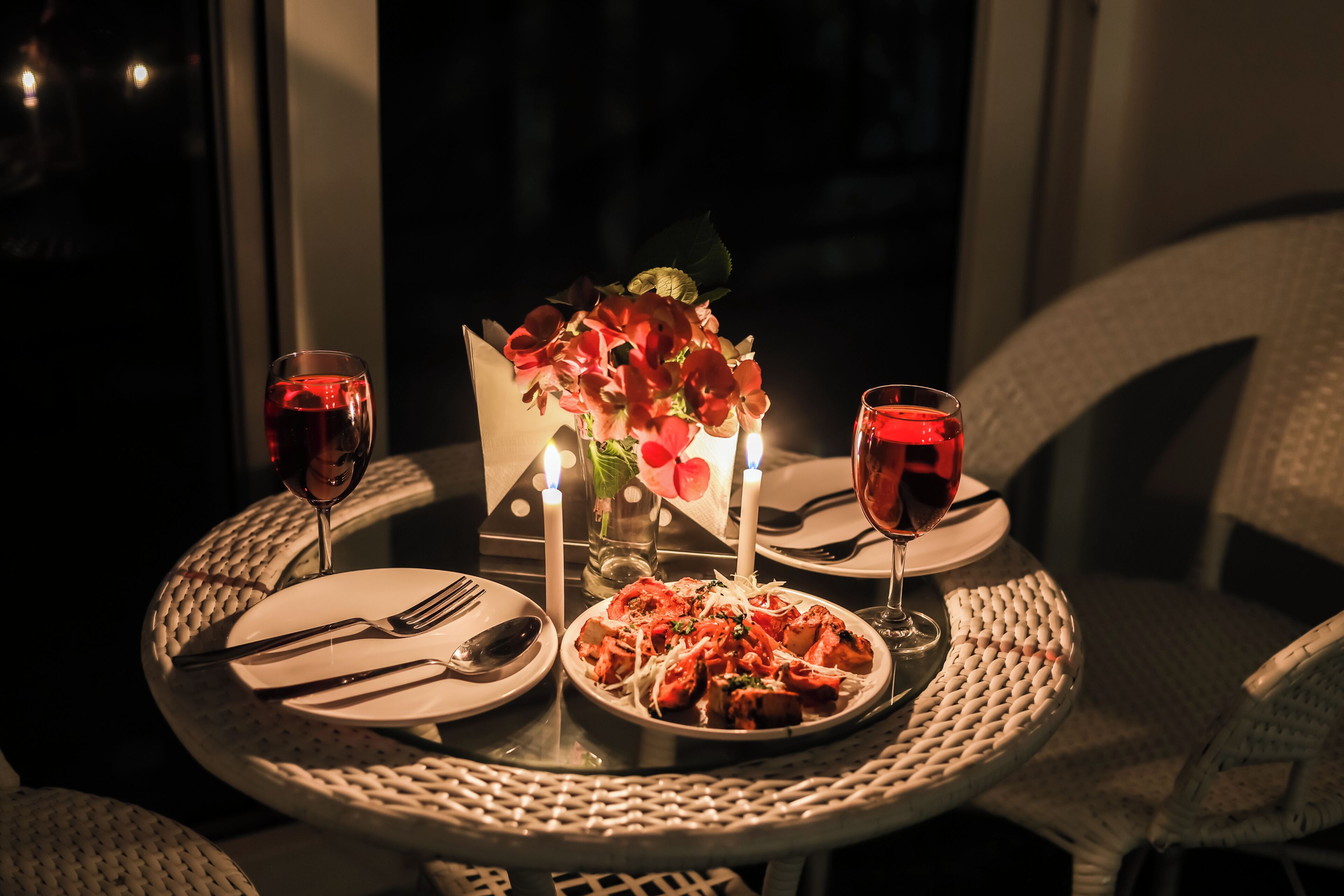 A dining table set with plates, cutlery, and glasses, accompanied by a candle holder with candles and a vase of flowers.