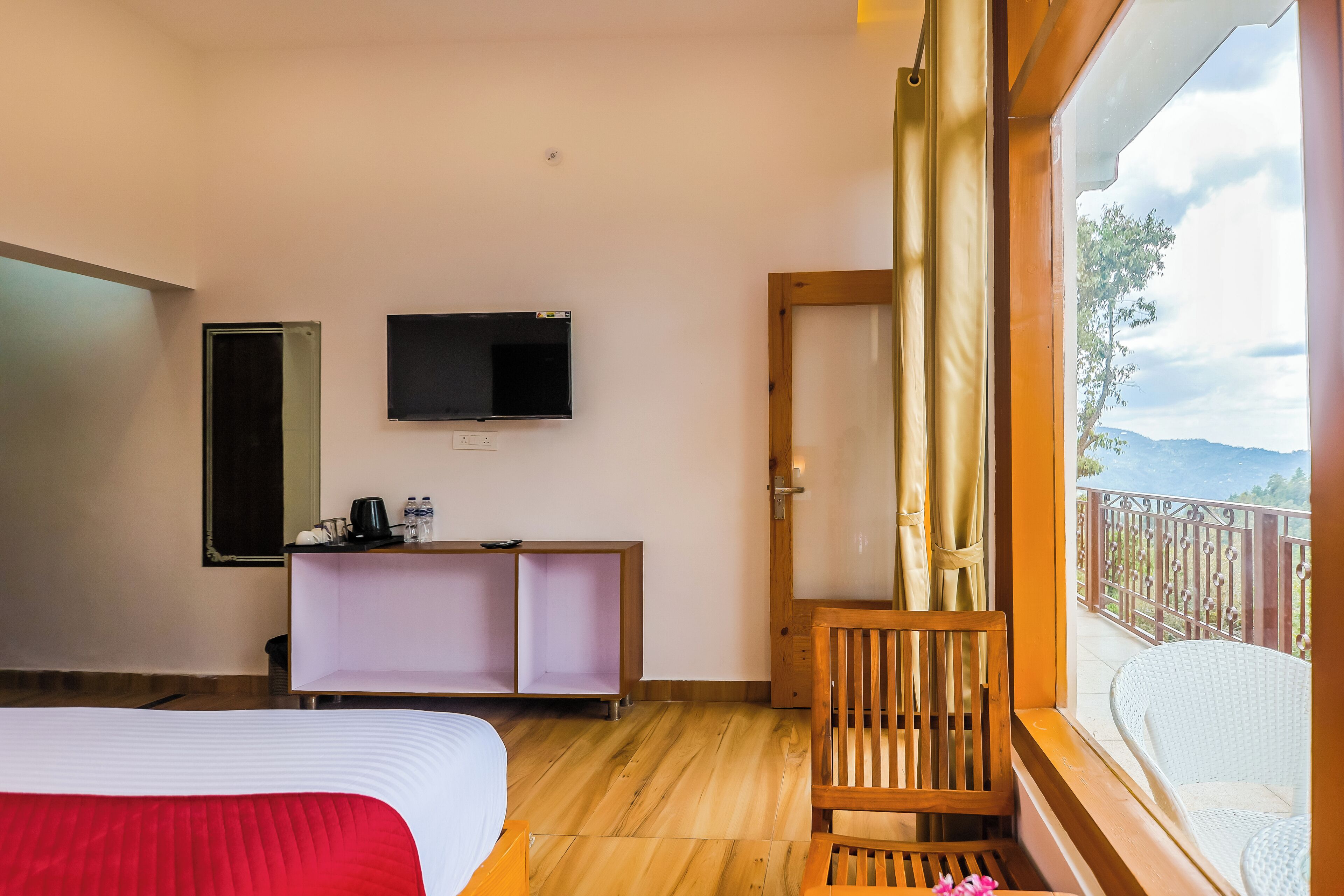 Une chambre d’hôtel avec un lit, une télévision, une chaise en bois, une petite table et un balcon avec vue.