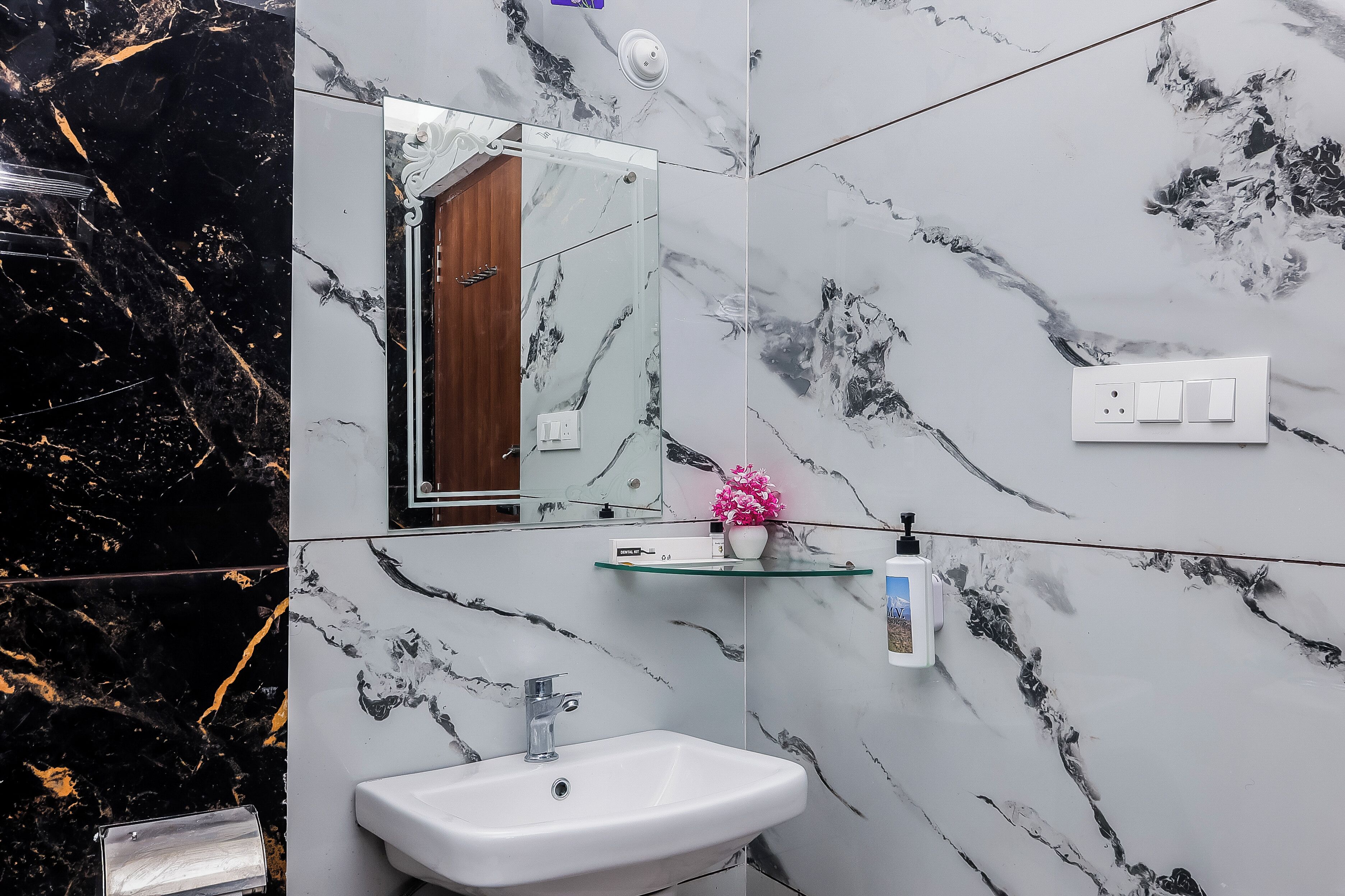 Un baño con salpicadero de mármol, un lavabo, un espejo y una estantería con artículos de aseo.