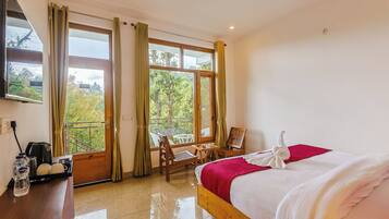 Habitación de hotel con cama, escritorio con tetera, una silla, una mesa y vistas a zonas verdes a través de amplios ventanales.
