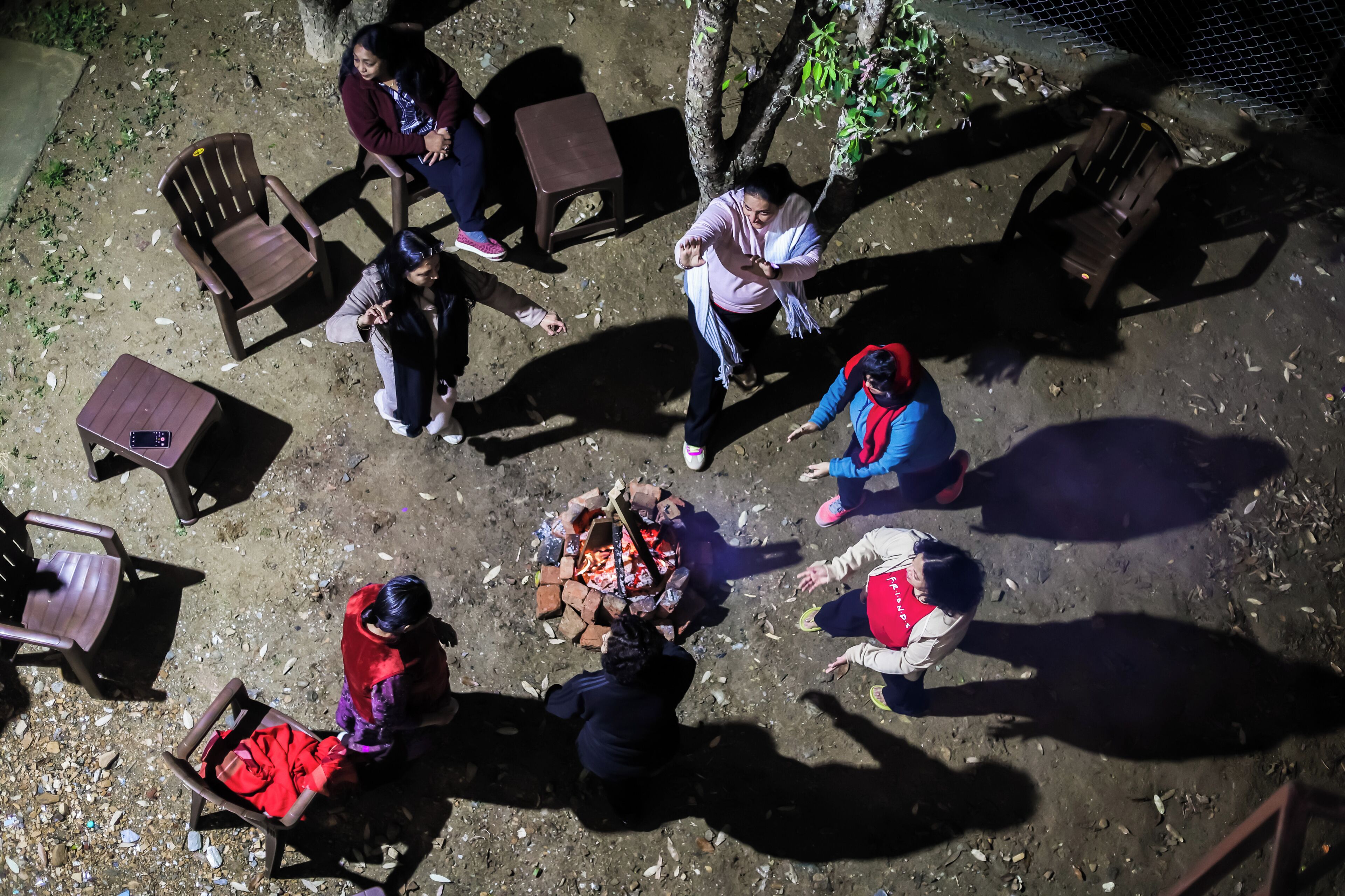 A group of people around a fire pit in an outdoor setting with chairs and tables.
