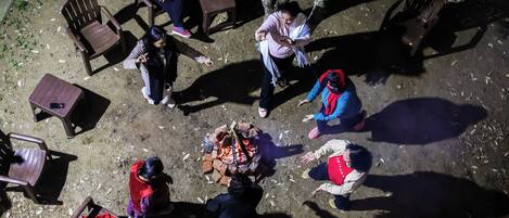 A group of people around a fire pit in an outdoor setting with chairs and tables.