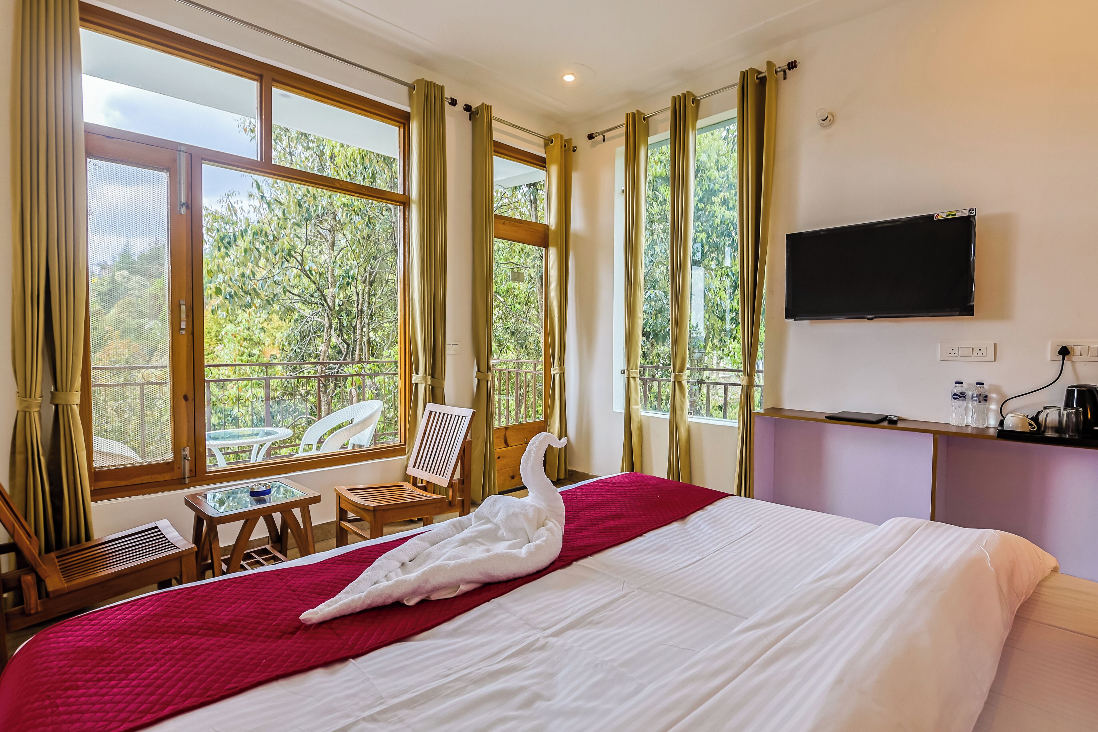 A hotel room with a bed, a TV, a balcony with chairs, and a table.