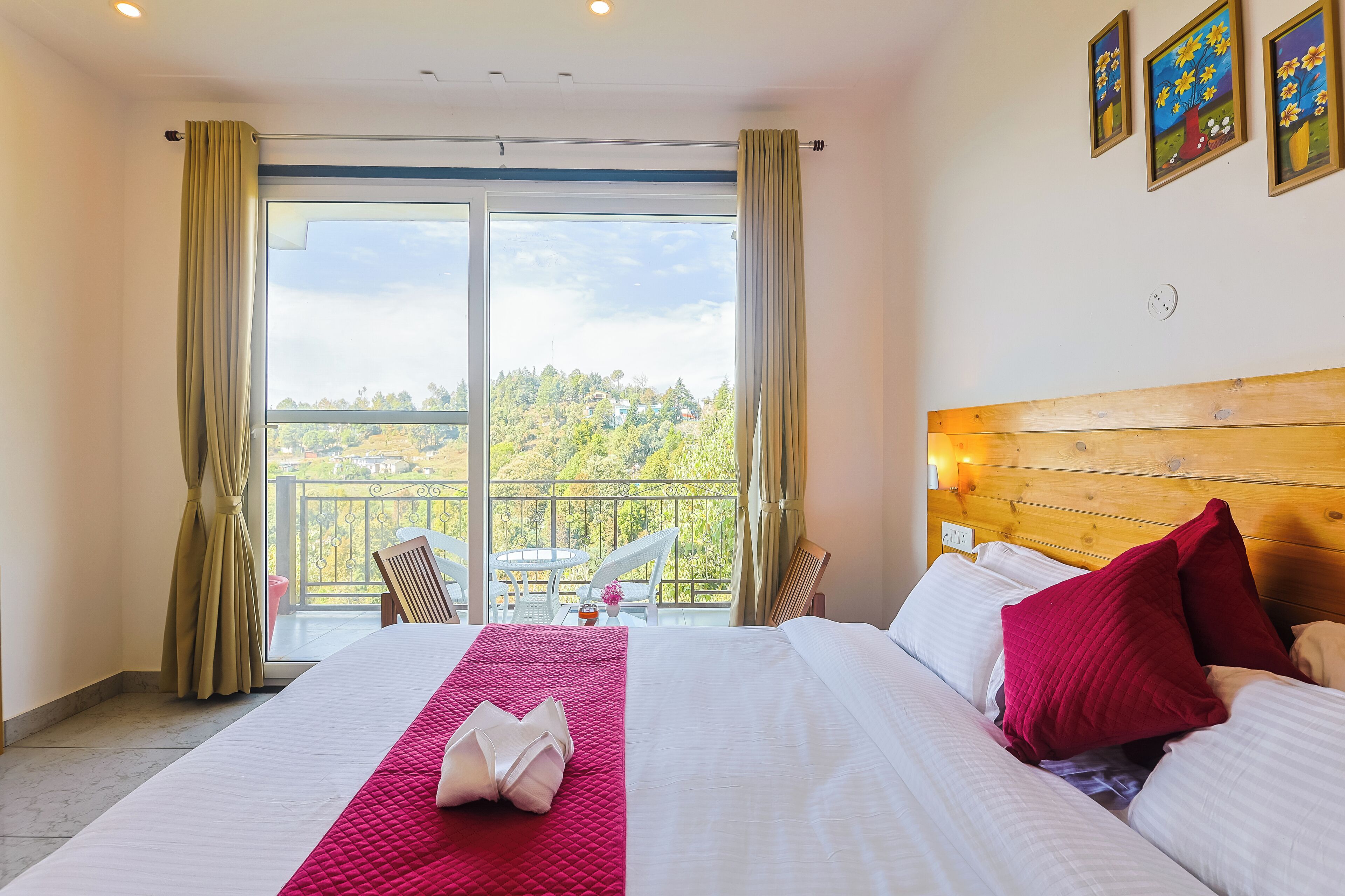 A hotel room with a bed, a balcony with a table and chairs, and a view of greenery.