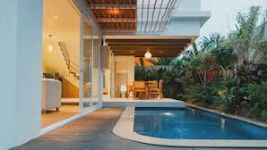 A modern pool area with a wooden deck, a seating area with chairs, and a staircase leading to an upper level. - Uma Avaya Villas Canggu (Canggu)