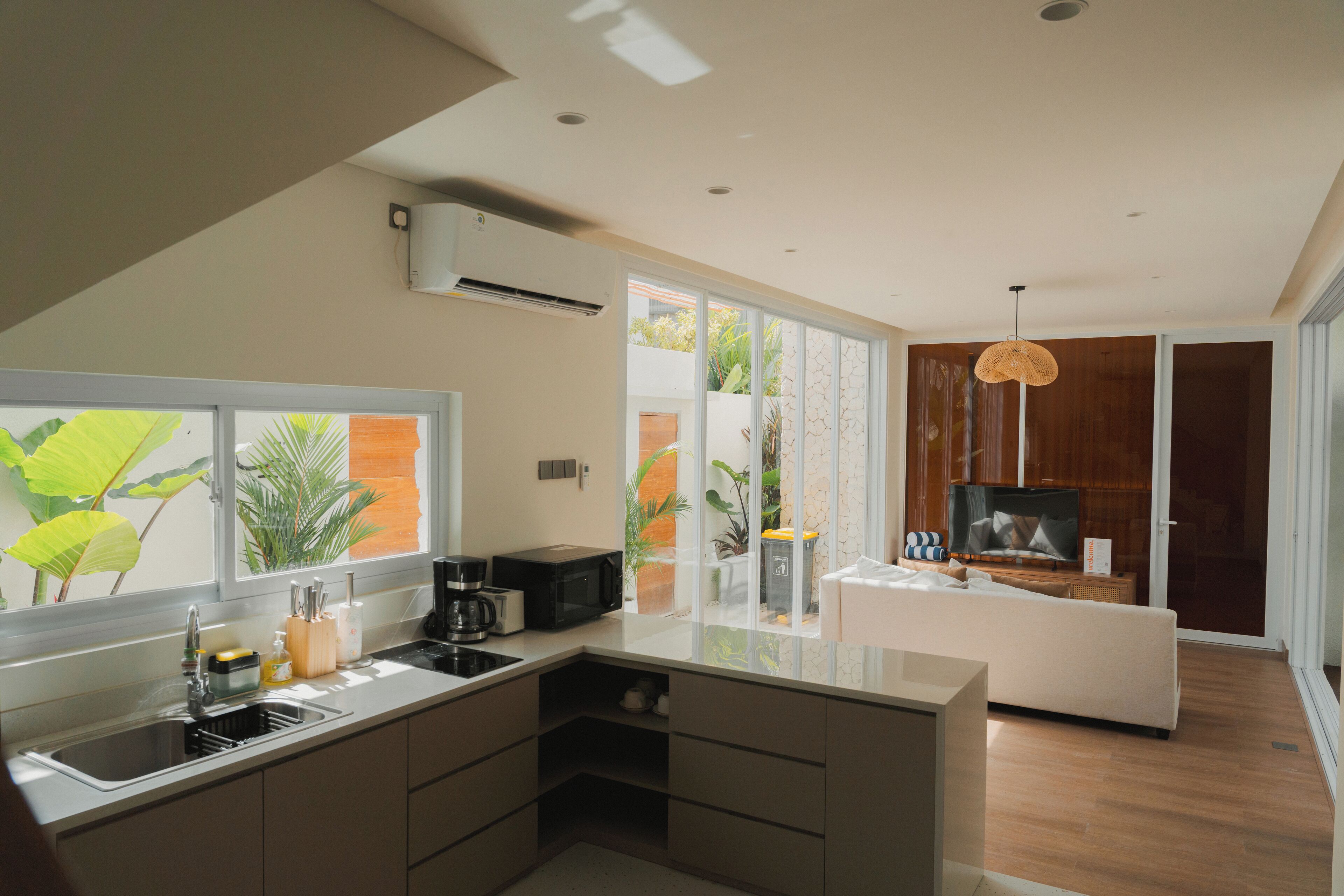 A modern kitchen with a built-in sink, a microwave, and a coffee maker. There is a large window with a view of greenery outside.