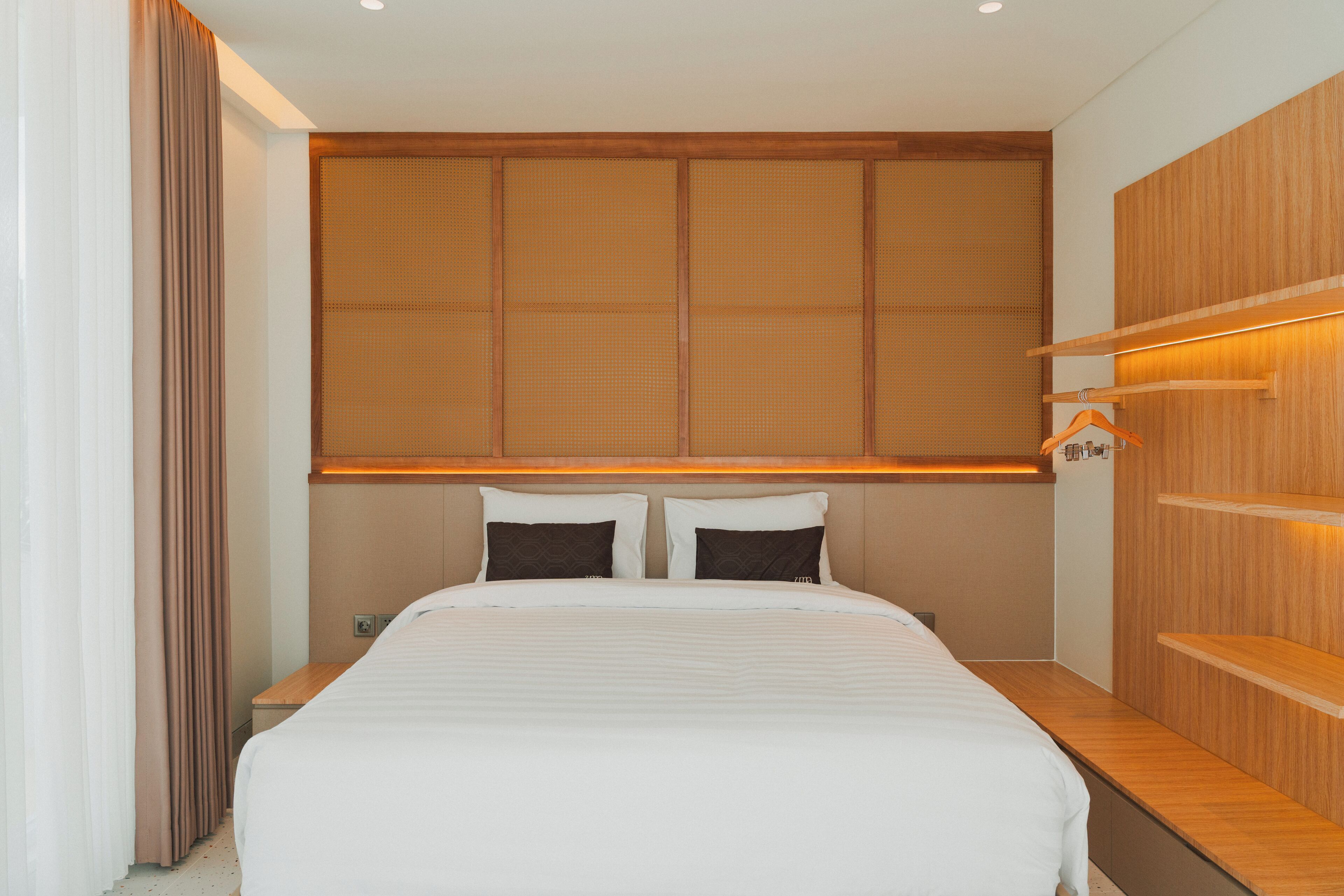 A modern hotel room with a large bed, wooden headboard, and built-in shelves.