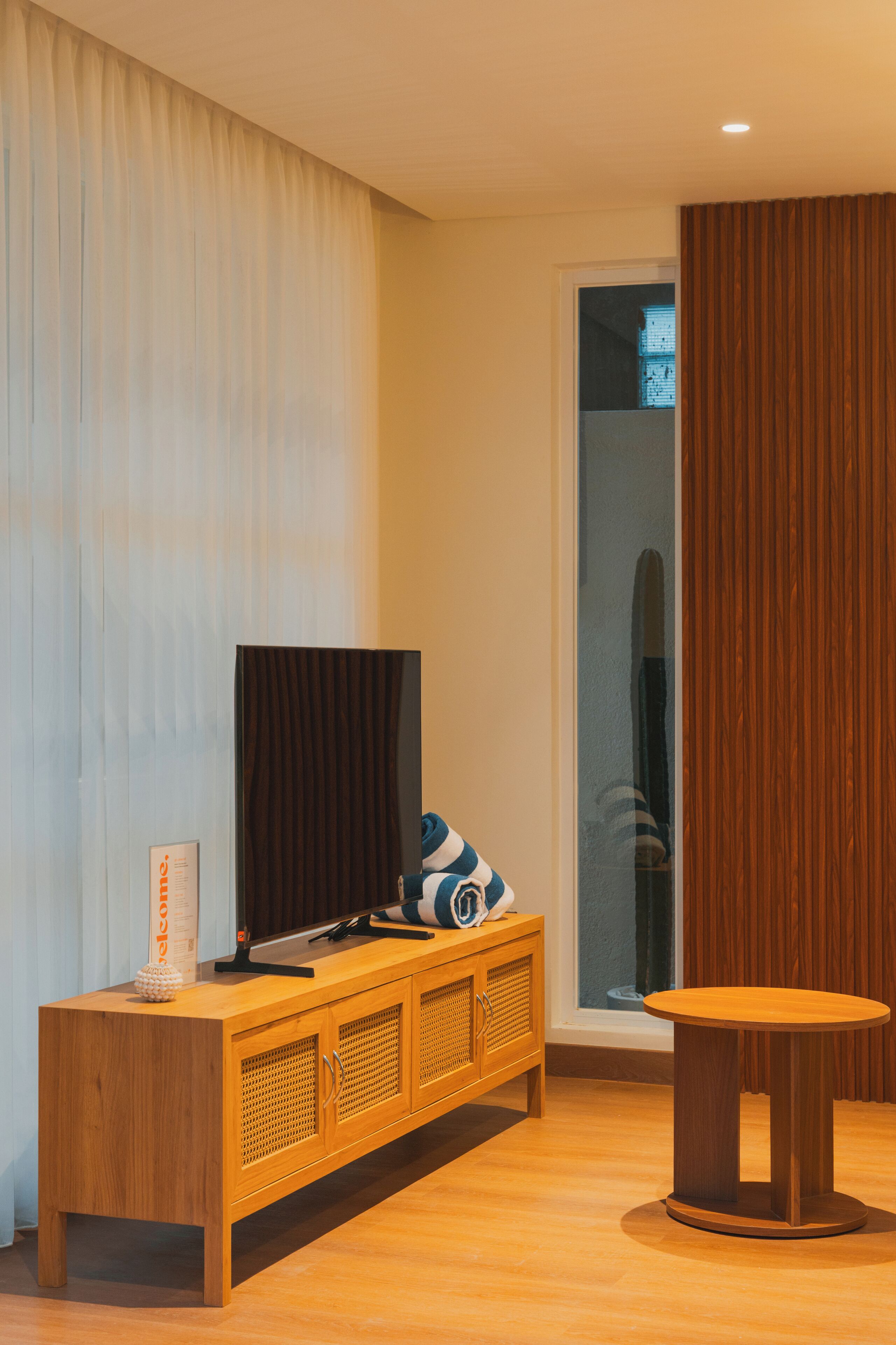 Una sala de estar moderna con un mueble bajo para televisor de madera, una mesa redonda y un ventanal con cortinas.